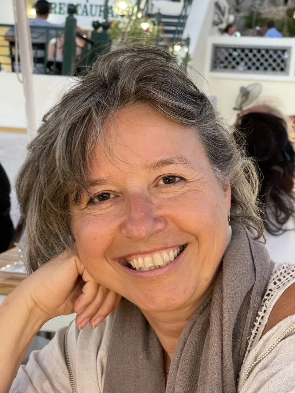 Porträt von Karin Daurer mit gewelltem, grau-braunem Haar, lächelnd, das Kinn auf die Hand gestützt