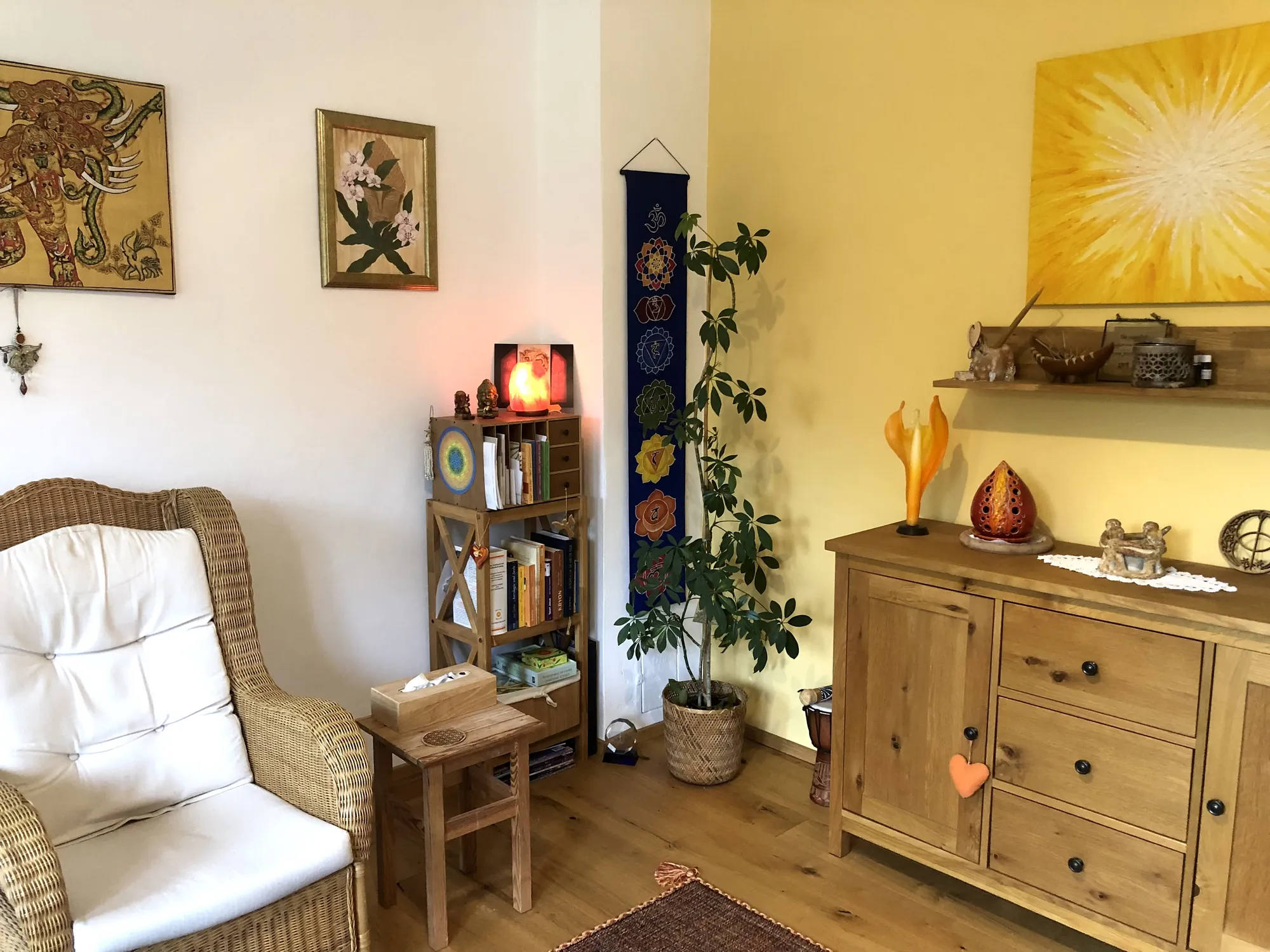 Der Praxisraum in Leobersdorf: heller Raum mit Korbsessel, Holzkommode, Salzkristall-Lampe, Pflanzen und Bildern an der Wand
