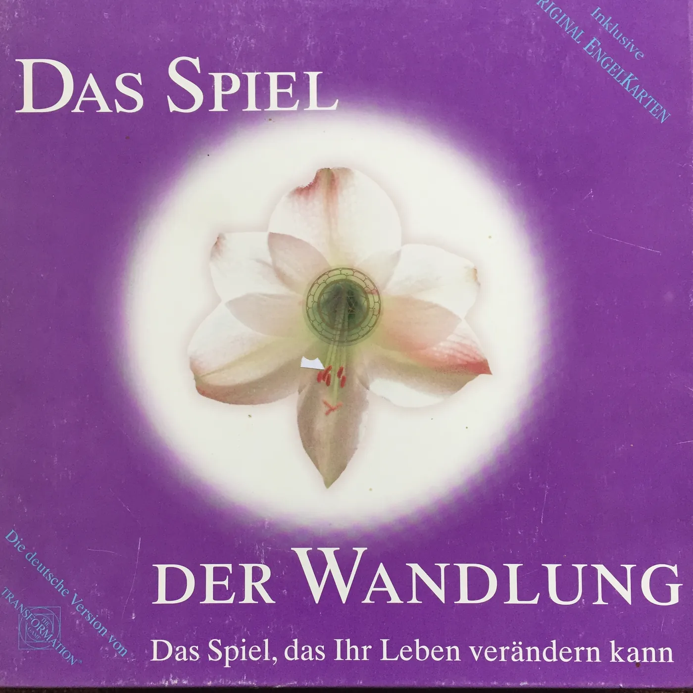 Violette Schachtel „Das Spiel der Wandlung – Das Spiel, das Ihr Leben verändern kann“ mit einer weißen Blüte in der Mitte